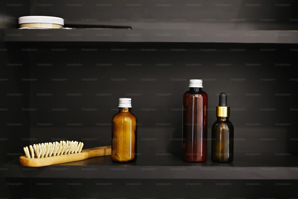 Brosse à cheveux en bois, ubtan pour la peau dans une bouteille en verre, shampooing, revitalisant, tonique en verre dans une salle de bain moderne sur étagère noire. Concept zéro déchet. Des essentiels naturels. Sans plastique