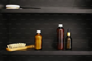Wooden hair brush, ubtan for skin in glass bottle, shampoo, conditioner, tonic in glass in modern bathroom on black shelf. Zero waste concept. Natural essentials. Plastic free
