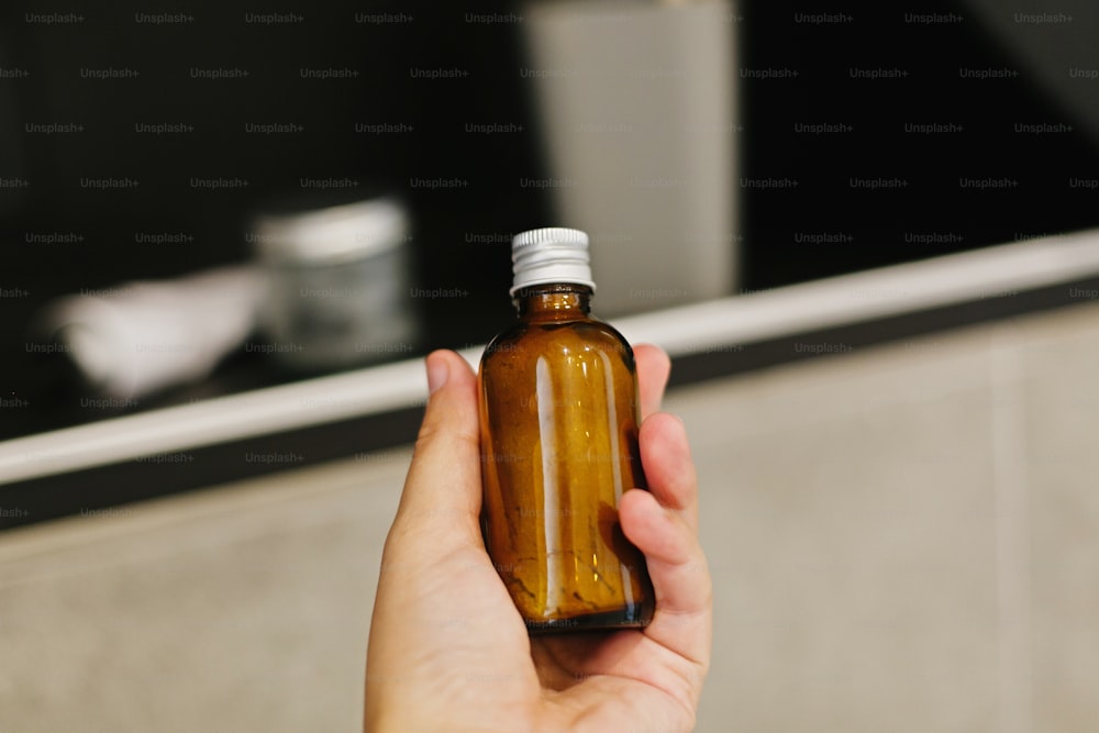 Hand holding ayurveda ubtan powder in glass in modern bathroom on background of stylish black shelf with natural organic essentials. Zero waste concept. Plastic free. Sustainable lifestyle