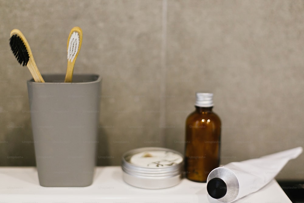 Bamboo toothbrush, ubtan for skin, solid shampoo in metal can, toothpaste in metal tube on white sink in modern bathroom. Zero waste concept. Plastic free. Sustainable lifestyle