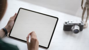 Cropped shot of female photographer working on blank screen tablet with stylus and camera on white table in simple co working space