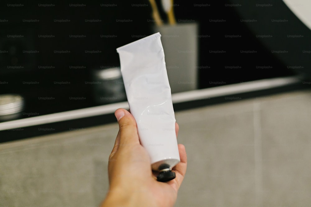 Hand holding natural deodorant or conditioner in metal tube in modern bathroom on background of stylish black shelf with plastic free natural organic essentials. Zero waste concept.