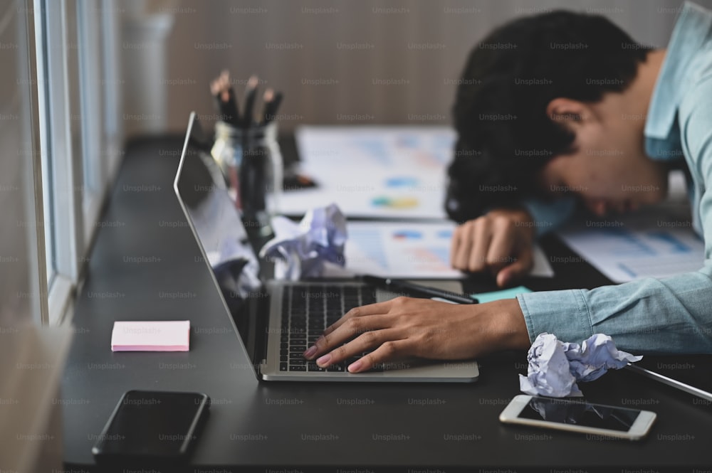 Photo of young businessman laid him head down on the working desk after feeling frustrated exhausted from work with modern working desk as background.