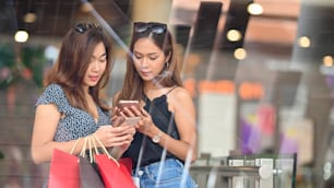 Beautiful women behind the supermarket glass wall, they talking/relaxing after finished shopping at the urban supermarket. Women relaxing/shopping with blurred background.