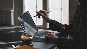 Junge Führungskraft zeigt mit elektrischem Stift auf das Computer-Tablet, während sie über die Arbeit am modernen Schreibtisch mit luxuriösem Büroraum als Hintergrund nachdenkt.