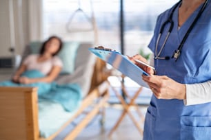 An unrecognizable doctor or nurse standing in hospital room, holding clipboard.