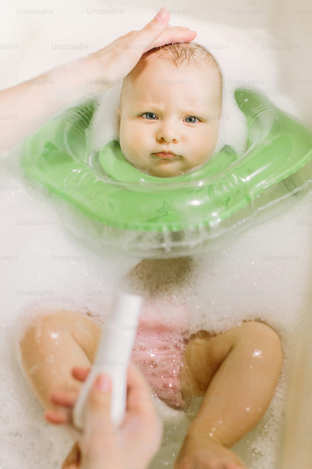 Bebê nadando com anel de natação de pescoço verde. mãe espreme xampu para fora do tubo