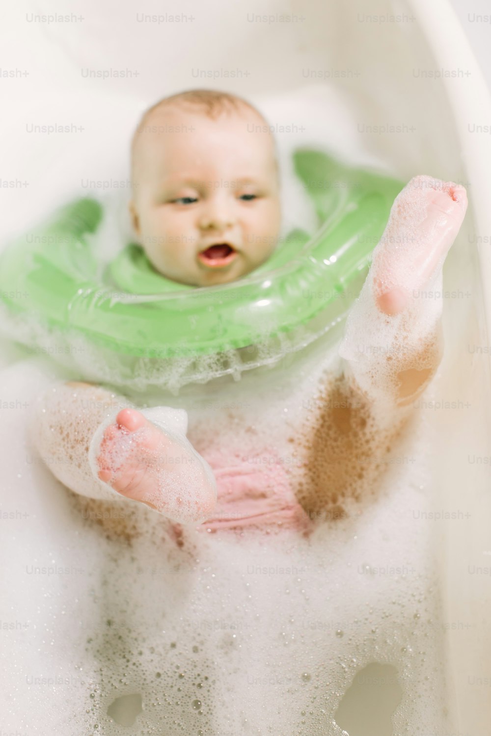 욕조에 녹색 목 수영 반지를 끼고 수영하는 아기