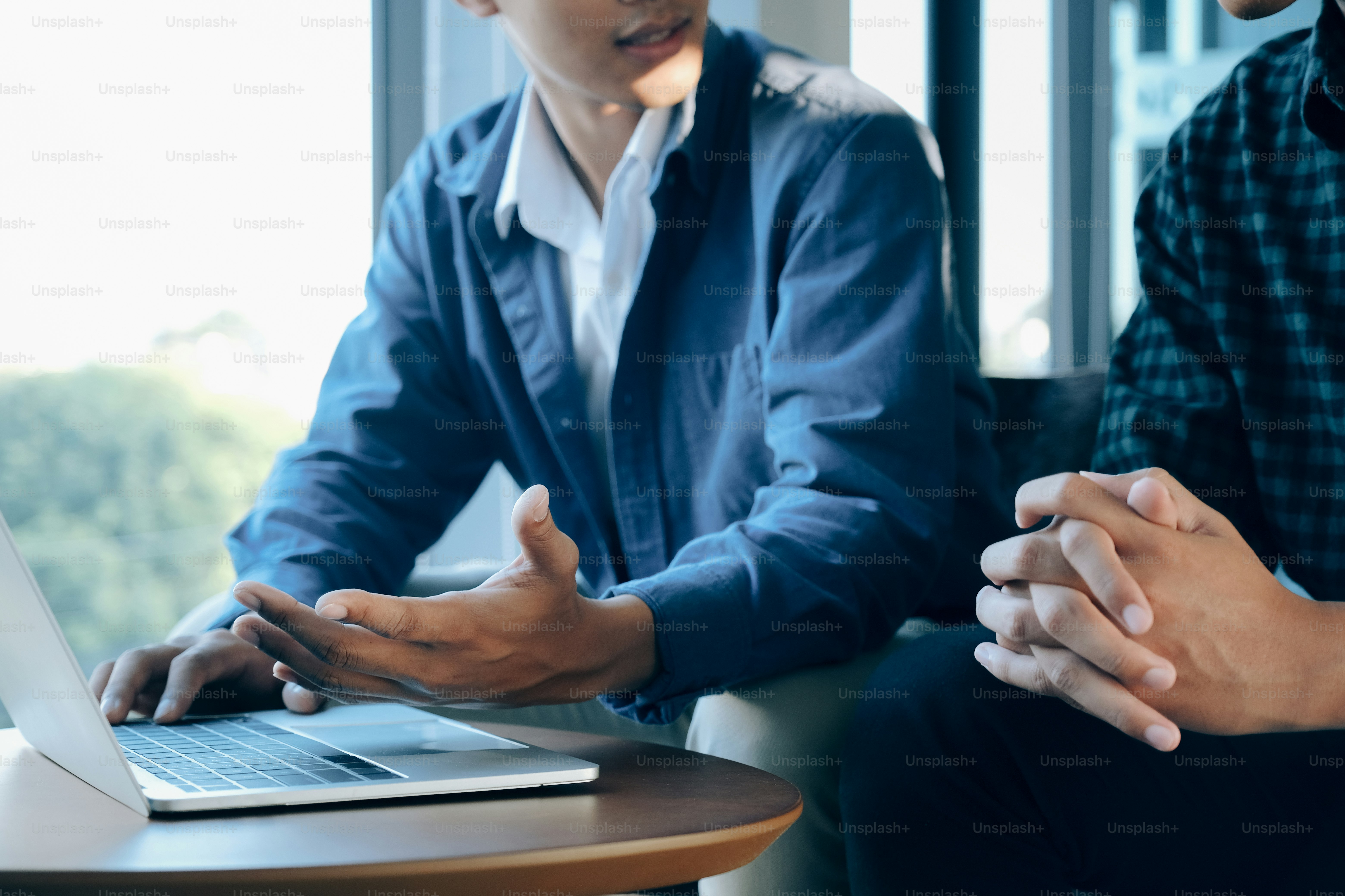 Closeup of two young businessmen using computer notebook at meeting ...