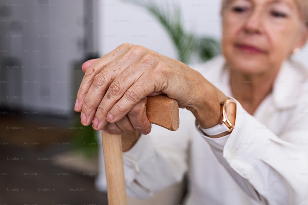 Hände einer alten Frau mit einem Stock, ältere Dame sitzt auf der Couch mit hölzernem Gehstock. Ausschnittaufnahme einer älteren Frau mit einem Stock in einem Altersheim