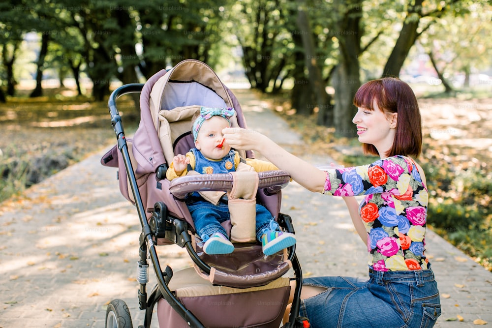 Mum spoon-feeds the child walking with baby stroller in park