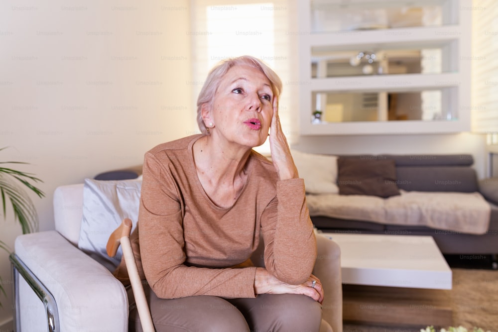 Mature woman holding her head with her hands while having a headache and feeling unwell. Senior woman with headache, pain face expression. Elderly woman having head pain migraine