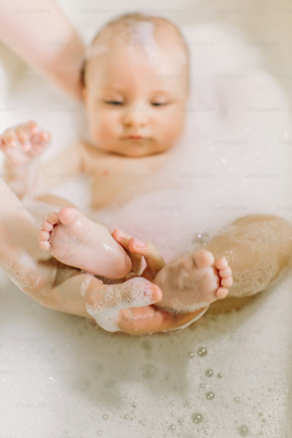 Happy laughing baby taking a bath playing with foam bubbles. Little child in a bathtub. Infant washing and bathing. Hygiene and care for young children. Newborn baby bathing