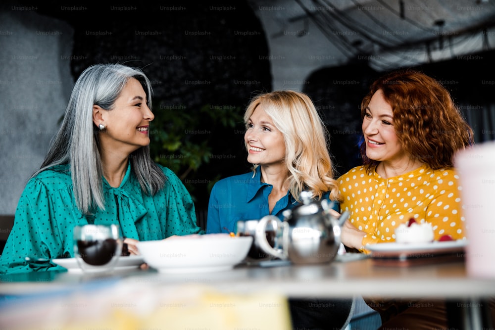 Tre belle donne gioiose sedute al tavolo nel ristorante - Foto stock. Concetto di amicizia femminile