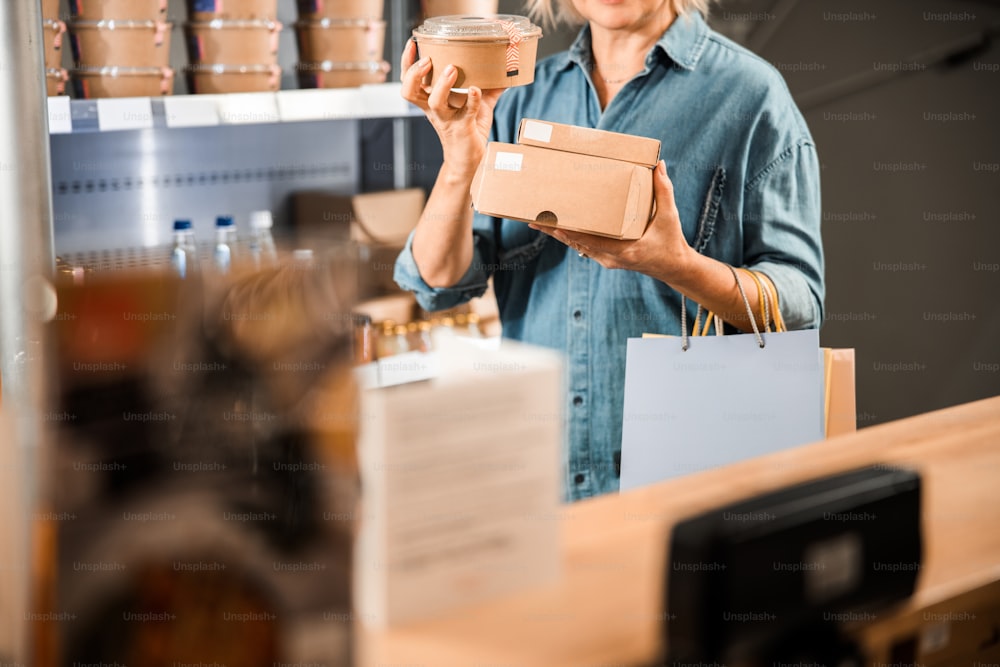 Cropped photo of mature lady choosing products and holding boxes in hands in store
