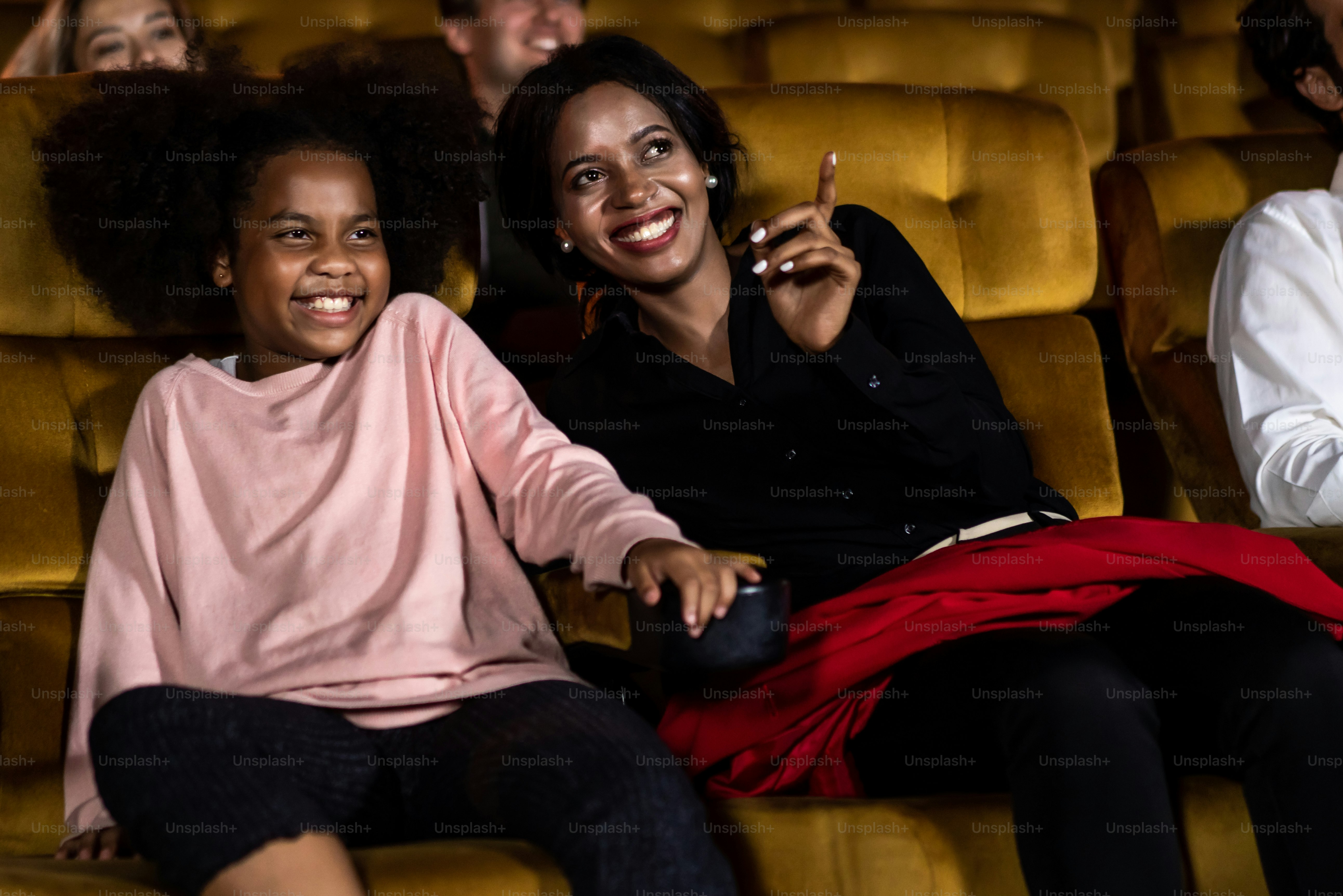 Woman enjoy to watch a movie with her daughter at the cinema smiling and laughing together