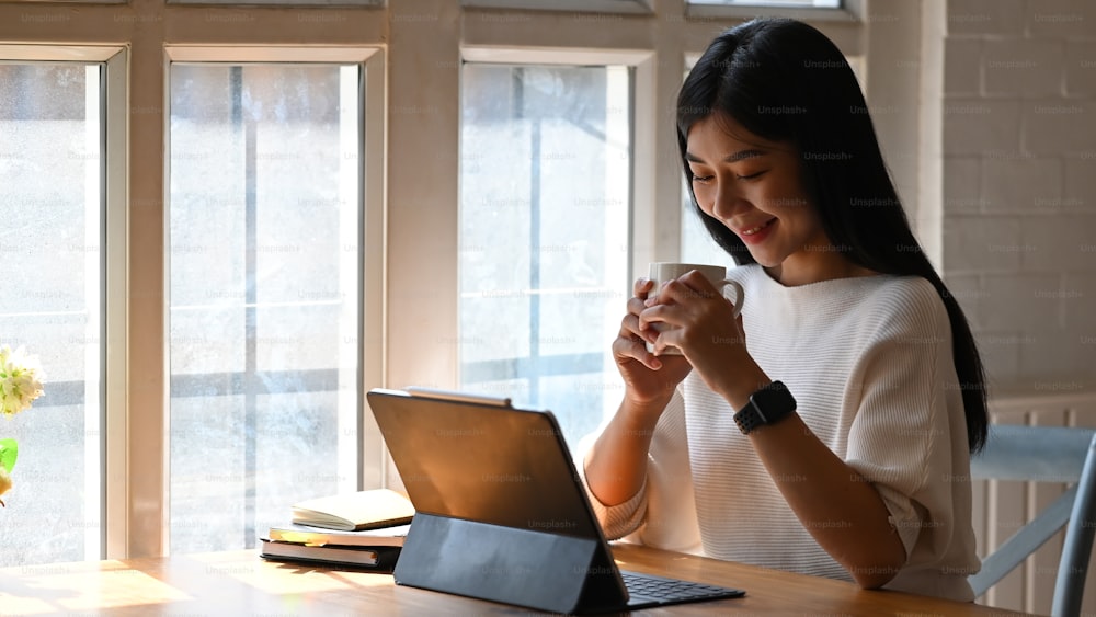 Coffee time concept, Young woman holding coffee mug in home office workplace.