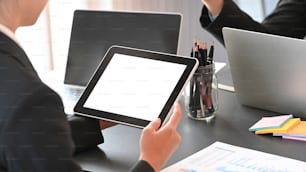 Behind shot of young businessman holding a white blank screen computer tablet while discussing about new business project at the modern meeting room.