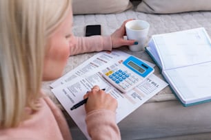 Candid shot of beautiful young Albino woman sitting with calculator and bills, doing paperwork. Hand woman doing finances and calculate on desk about cost at home office.Concept finances and economy