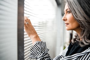 Calm attractive adult woman touching the blinders on her office window and looking out