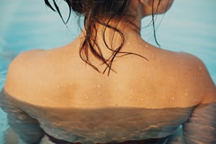 Beautiful young woman relaxing in pool, shoulder with water drops close up. Back view of brunette girl with wet skin with goosebumps. Summer vacation. Enjoying summer holiday, swimming in pool