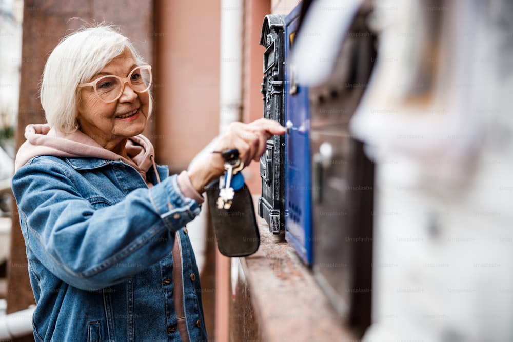 Sorridente seniour fêmea está usando chave para abrir caixa de correio na rua. Banner do site