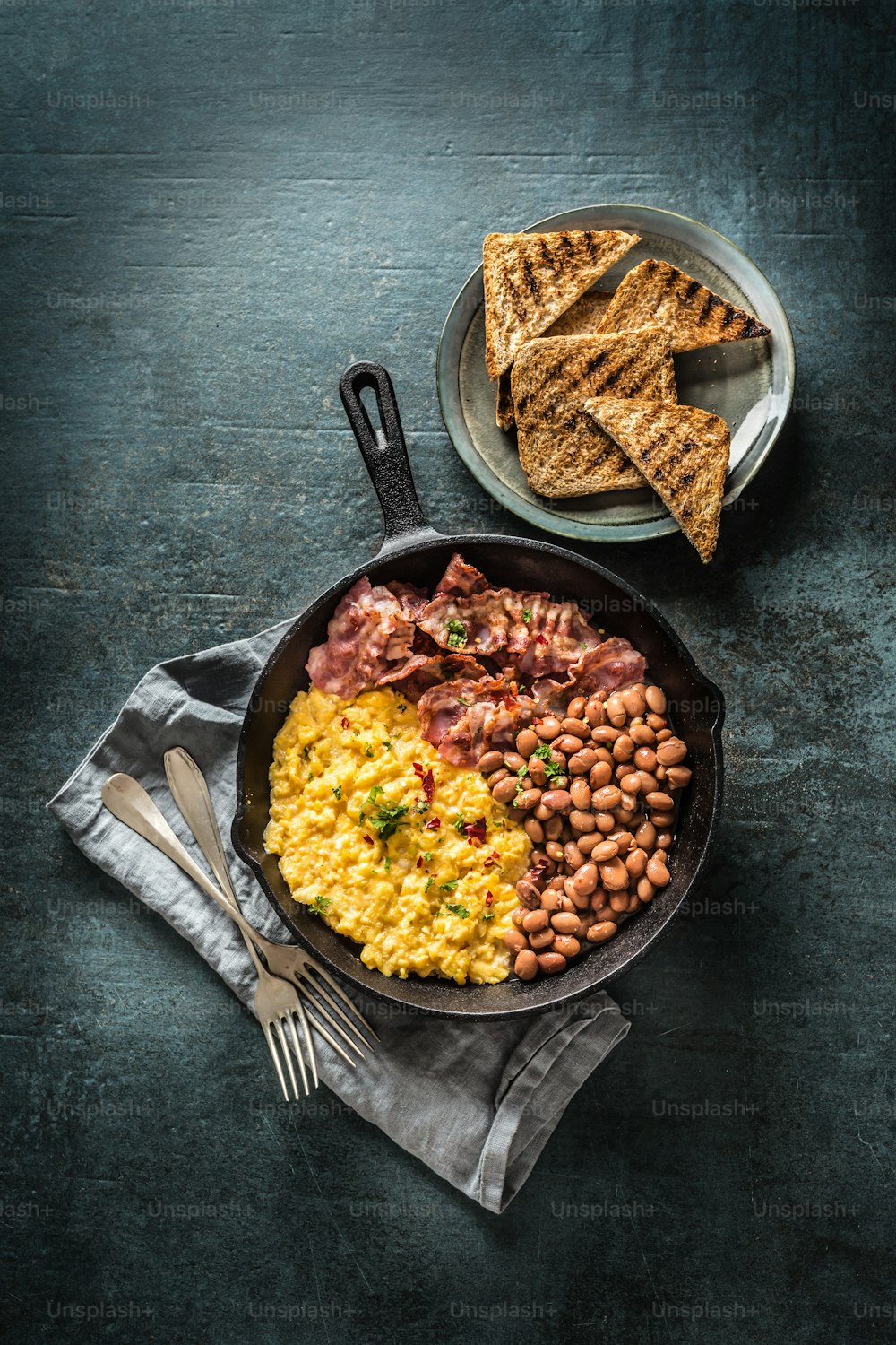 English breakfast scrambled eggs grilled bacon beans and toast bread - Top of view.