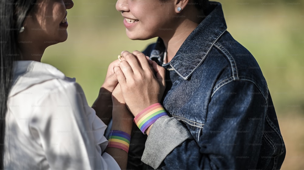 Cropped shot of young LGBT Lesbian holding her lover hand at the beautiful park with the blurred green grass as background. LGBT Happiness couple concept.