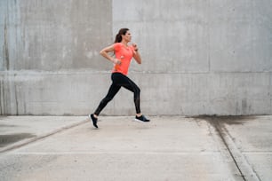 Portrait of a fitness woman running on the street against grey background. Sport and healthy lifestyle.