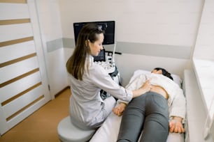 Ultraschall in der Physiotherapie. Junge Therapeutin mit Ultraschallscanner bei weiblichen Patienten im unteren Rückenbereich. Rücken- und Nierenultraschall.