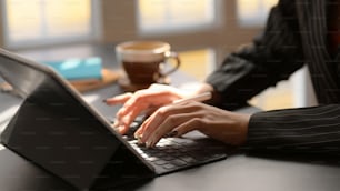 Side view of  female typing on digital tablet with coffee cup and other office supplies on black desk in modern workplace