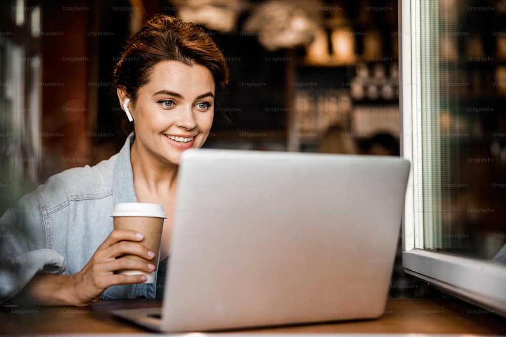 Cheerful lady is sitting in cafe and using notebook and earphones. Website banner