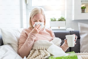 Resfriado e gripe. Retrato de mulher doente pega frio, sentindo-se doente e espirrando em papel wipe. Menina insalubre coberta de cobertor limpando o nariz. Conceito de Saúde. Menina albina doente e bebendo bebida quente
