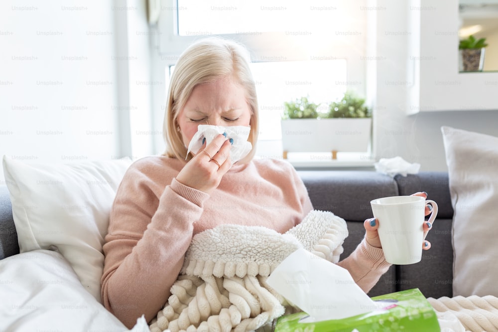 Cold And Flu. Portrait Of Ill Woman Caught Cold, Feeling Sick And Sneezing In Paper Wipe. Unhealthy Girl Covered In Blanket Wiping Nose. Healthcare Concept. Albino girl sick and drinking hot beverage