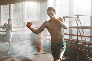 Homem bonito malhando com banda de resistência no ringue de boxe na academia. Músculos do braço e das costas perfeitamente moldados.