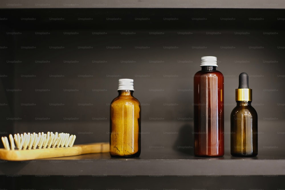 Zero waste concept. Natural essentials. Plastic free wooden hair brush, ubtan for skin in glass bottle, shampoo, conditioner, tonic in glass in modern bathroom on black shelf.