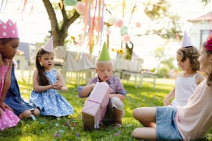Down syndrome child with friends on birthday party outdoors in garden, opening presents.