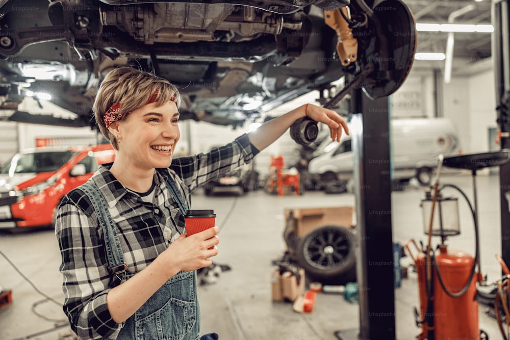 Joven mecánico feliz sosteniendo una taza de café de papel