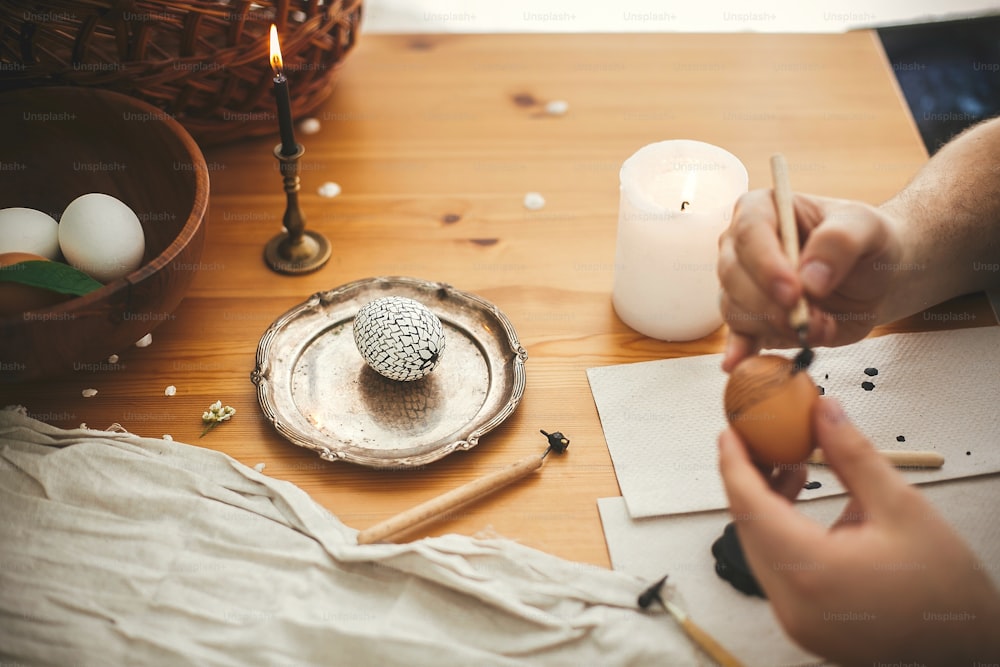 Oeuf de Pâques avec ornement moderne et peinture Oeuf de Pâques à la cire chaude sur fond de table en bois rustique avec bougie, panier, verdure. Joyeuses Pâques. Pysanka traditionnel ukrainien.