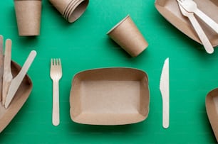 Disposable eco friendly food packaging. Brown kraft paper food containers on green background. Top view, flat lay.