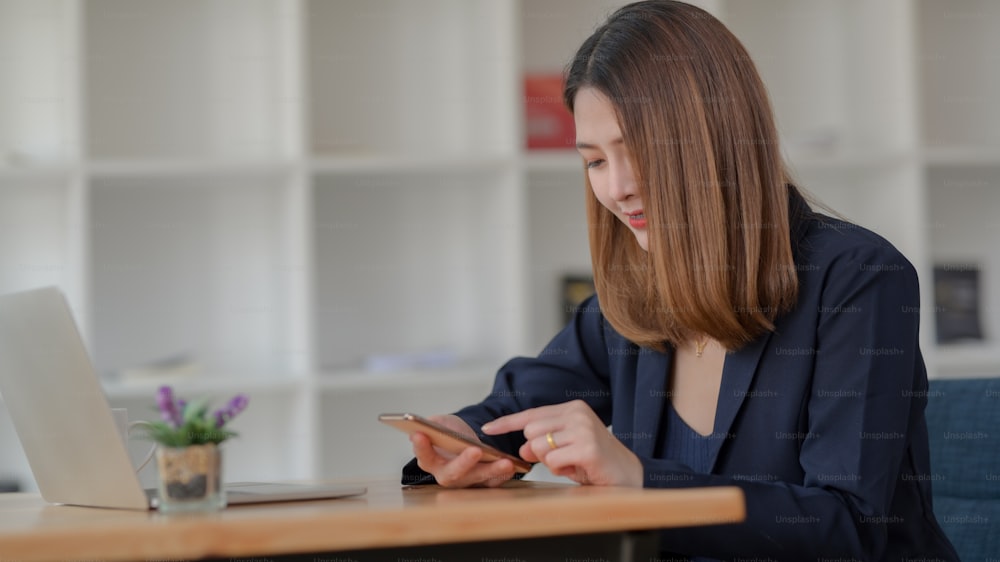 Abgeschnittene Aufnahme einer Geschäftsfrau Machen Sie eine Pause und entspannen Sie sich mit dem Smartphone, während Sie im modernen Büroraum sitzen