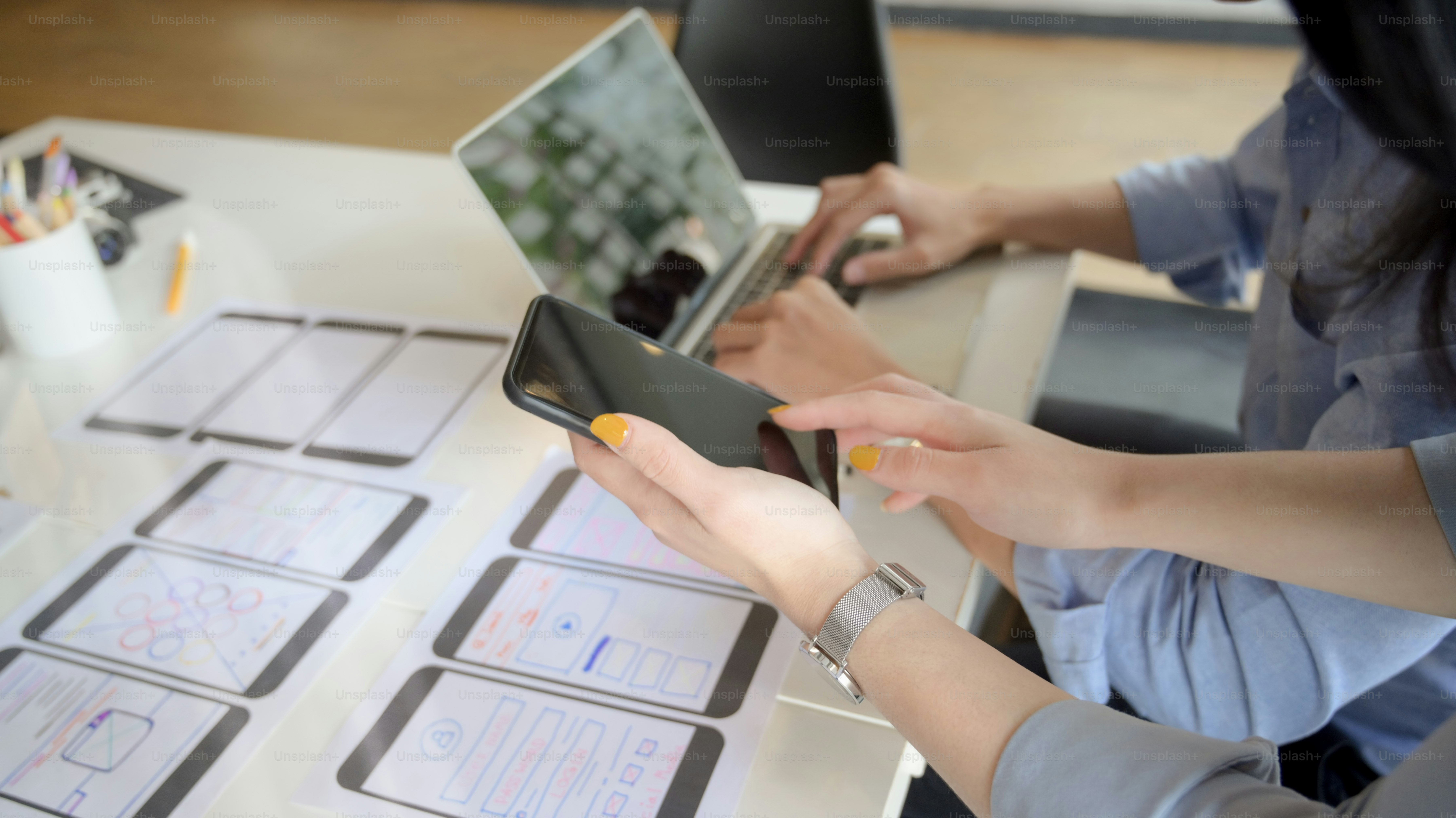 Close-up view of young female UI designer showing smartphone to her co-worker for the project
