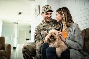 Happy army soldier and his wife communicating while relaxing at home with their dog.