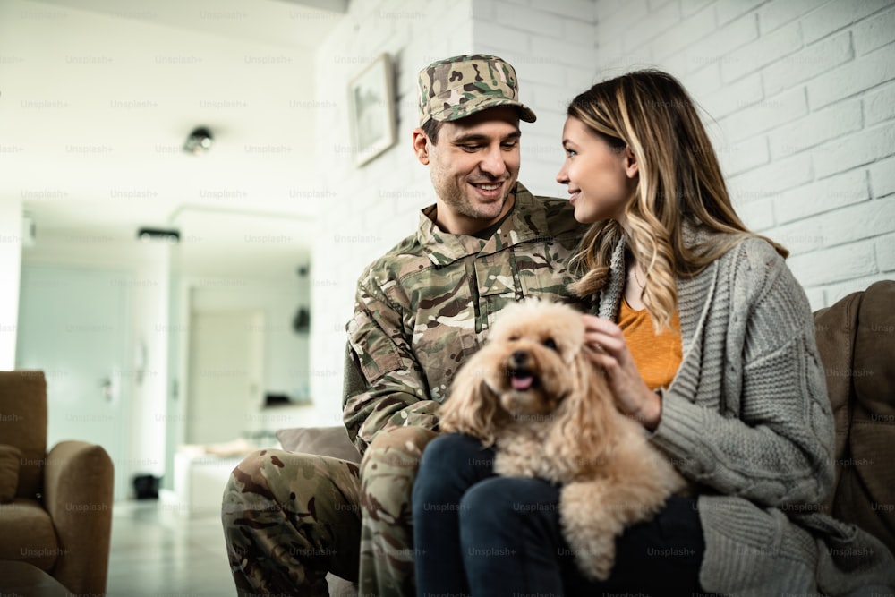 Soldat de l’armée heureux et sa femme communiquant tout en se relaxant à la maison avec leur chien.