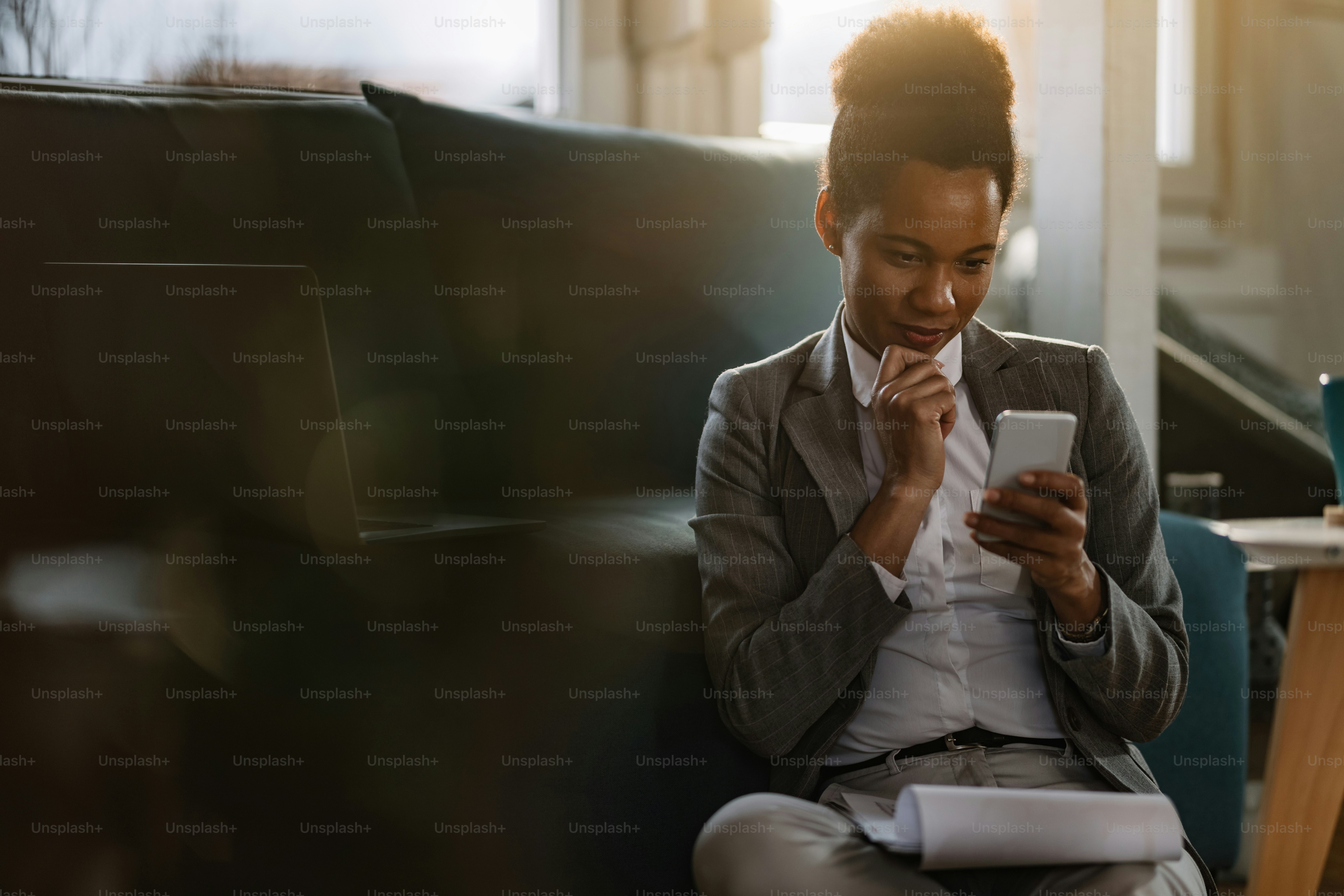 Smiling black entrepreneur texting on mobile phone while working on ...