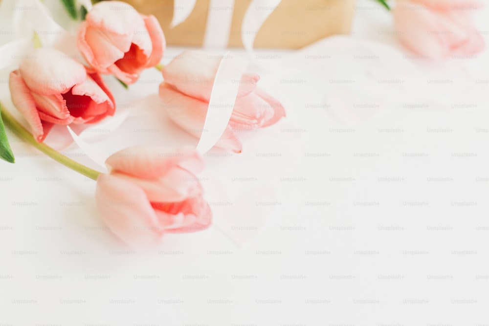 Tulipes roses avec ruban et boîte cadeau sur fond blanc, espace pour le texte. Image douce et élégante de fleurs printanières. Bonne journée de la femme. Maquette de carte de voeux. Bonne fête des mères.  Bonjour le printemps