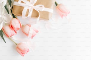 Feliz día de la mujer. Los tulipanes rosados son planos con cinta y caja de regalo sobre fondo blanco, espacio para texto. Imagen suave y elegante. Maqueta de tarjeta de felicitación. Feliz día de la madre. Hola primavera