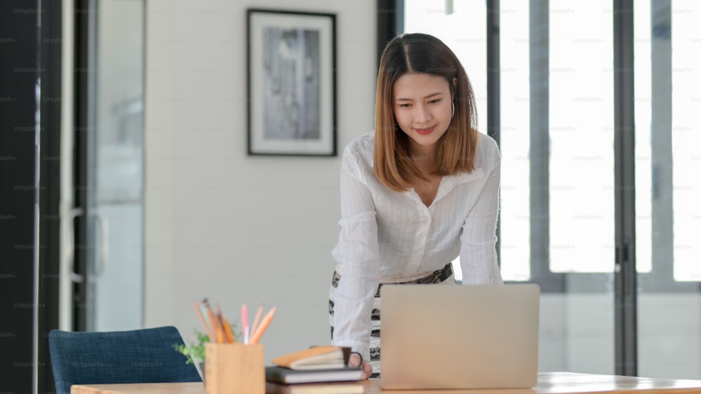 Ausschnittaufnahme einer Geschäftsfrau, die am Laptop arbeitet, während sie an ihrem Arbeitsplatz in einem komfortablen Büroraum steht