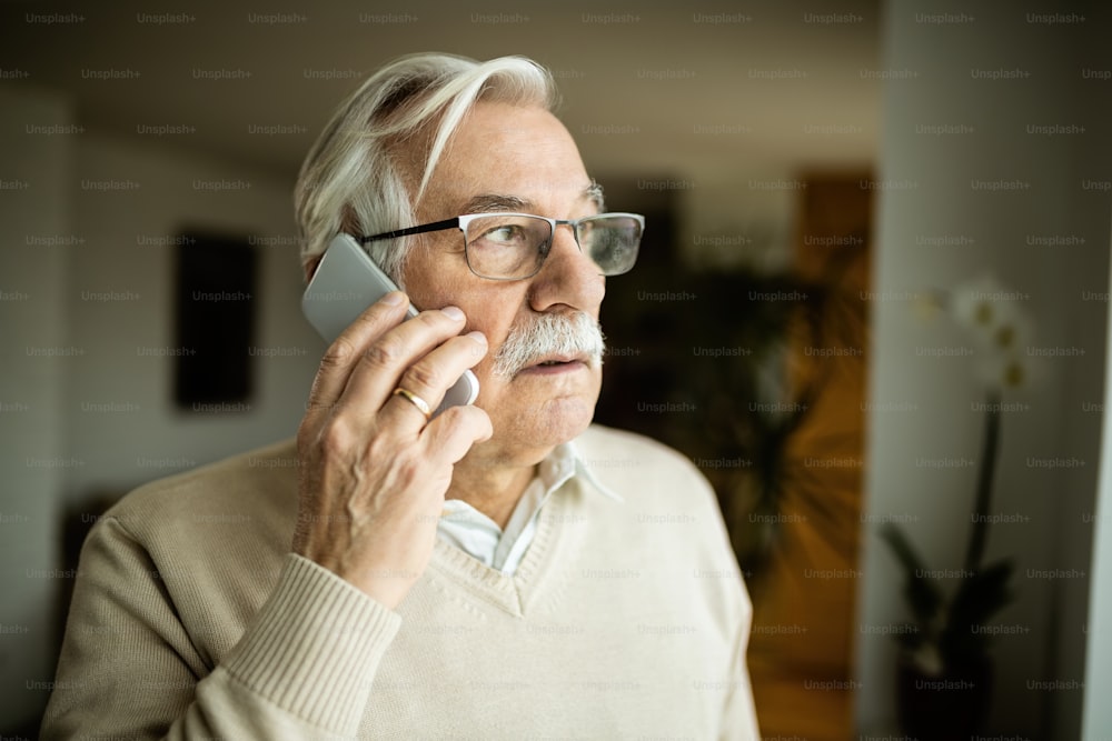 Nachdenklicher älterer Mann, der wegschaut, während er zu Hause telefoniert.