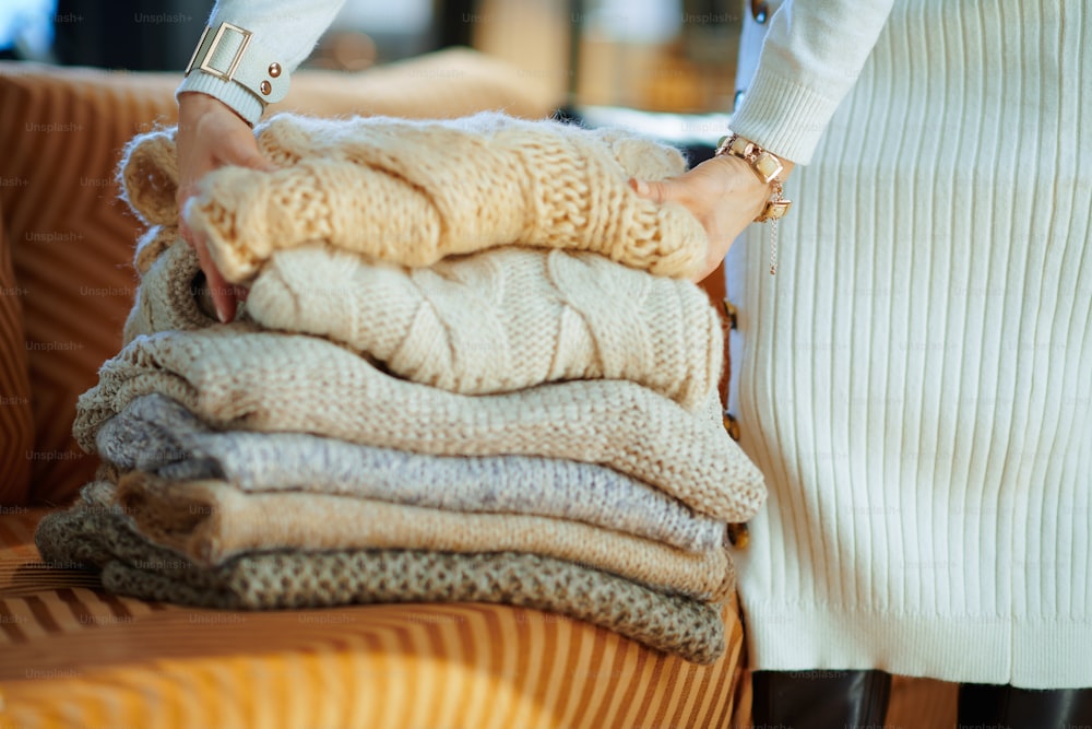 晴れた冬の日のモダンな家で、白いセーターとスカートを着た中年の女性の接写、収納用のソファ折りたたみセーターの近く。